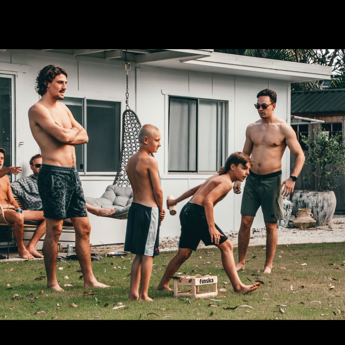 people outside at a beach house playing finska game on the lawn