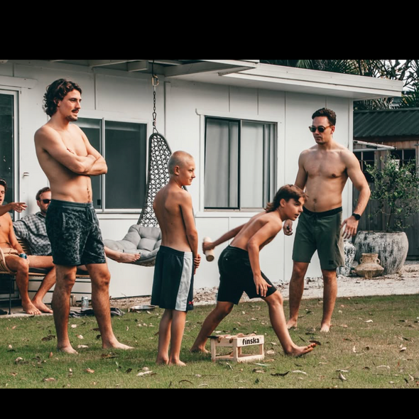 people outside at a beach house playing finska game on the lawn