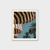 Framed artwork of striped awnings and palm trees against a blue sky.