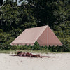 Beige tent set up on a sandy area with greenery in the background