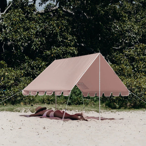 Beige tent set up on a sandy area with greenery in the background