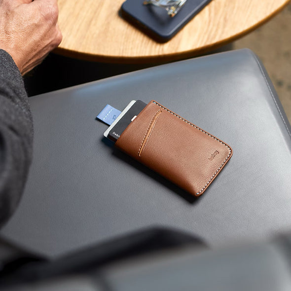 Brown leather wallet with a card on a gray surface, with a blurred background of a person sitting at a table.