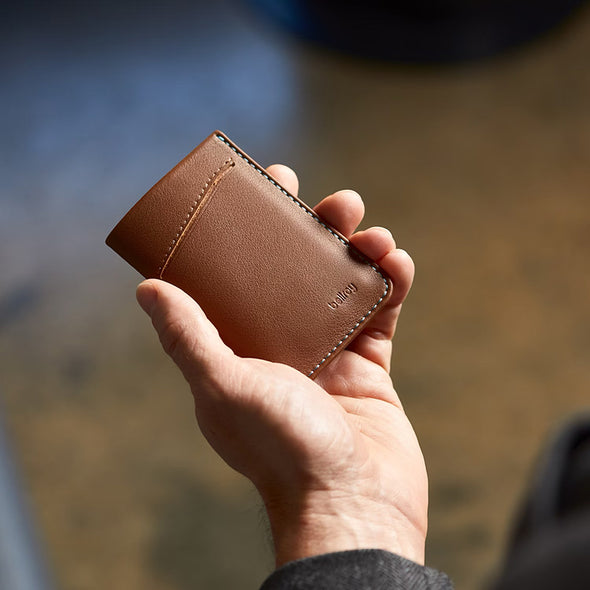 Hand holding a brown leather wallet with a blurred natural background