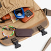 Close-up of a beige bag with a phone, wallet, and colorful beaded bracelet on a white background