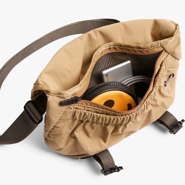 Beige waist bag with a strap, open to reveal a smartphone and headphones inside on a white background.