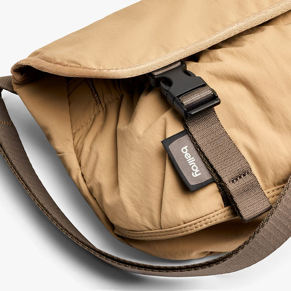 Close-up of a tan bag with a brown strap and visible brand label on a light gray background