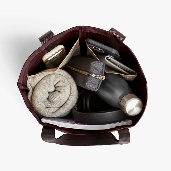 Open Bellroy City Tote Burgundy with rolled socks, black flask, and other items on a white background