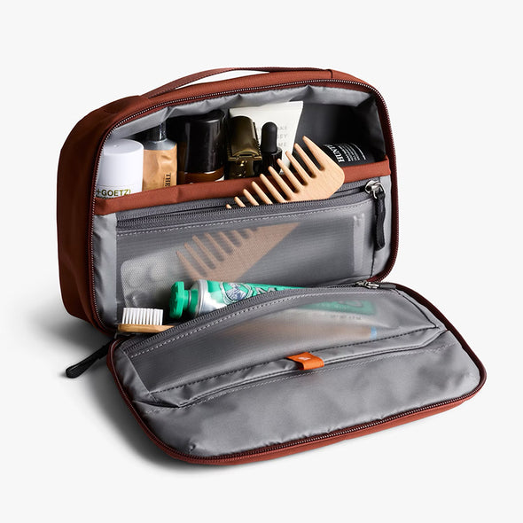 Open toiletry bag with various travel items on a white background