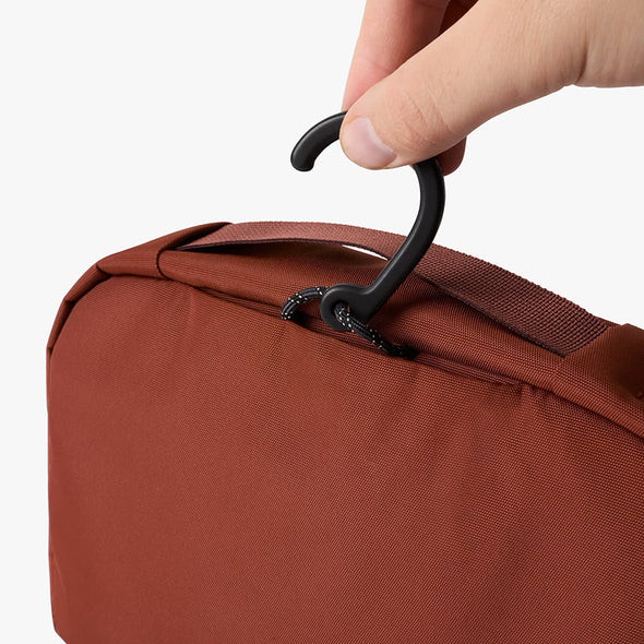 Brown bag with a black hook being held by a hand on a white background