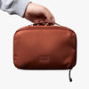 Brown travel pouch held by a hand with 'bellroy' branding on a white background