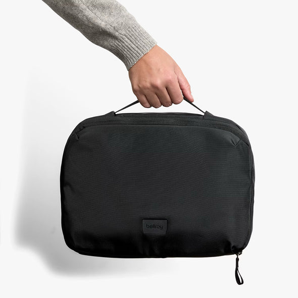 Black travel toiletry bag held by a person's hand on a white background