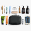 Collection of grooming products including bottles, tubes, and a black toiletry bag on a white background.