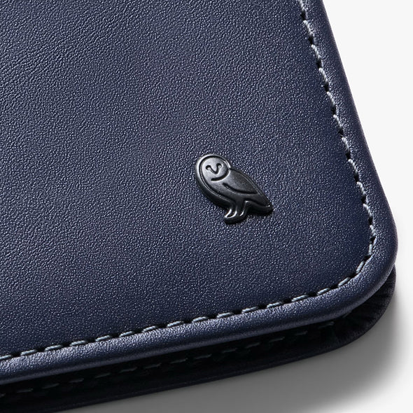 Close-up of a navy blue leather wallet with an owl emblem on a light gray background