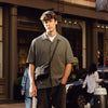 Man standing on a city street wearing a green shirt and dark pants.
