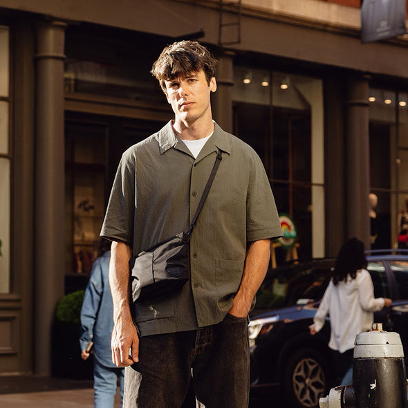 Man standing on a city street wearing a green shirt and dark pants.
