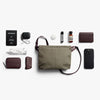 Collection of travel items including a green bag, phone, wallet, and bottles on a white background.