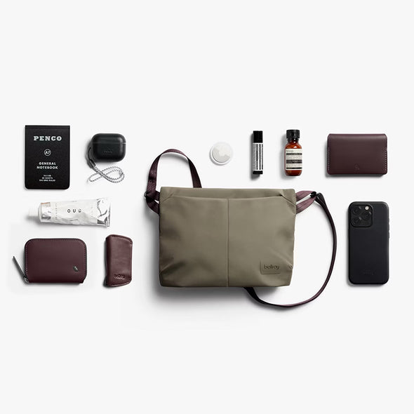 Collection of travel items including a green bag, phone, wallet, and bottles on a white background.