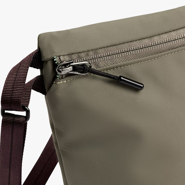 Close-up of a green bag with a zipper and brown strap on a white background