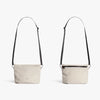 Two beige crossbody bags with black straps on a white background