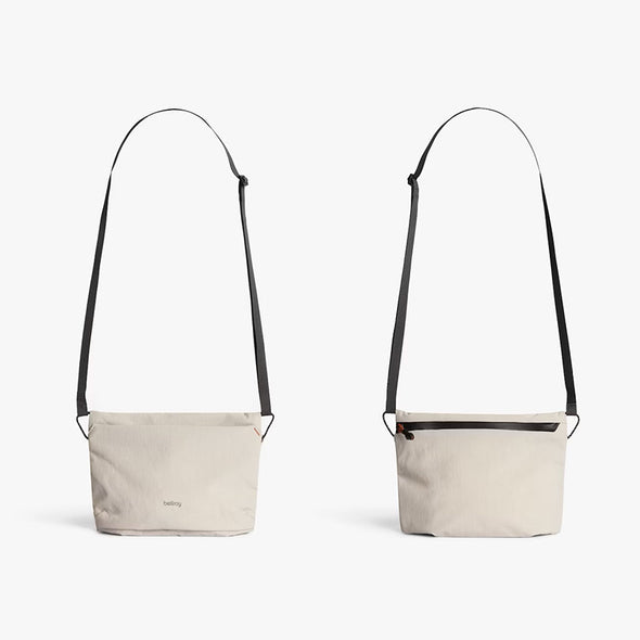 Two beige crossbody bags with black straps on a white background
