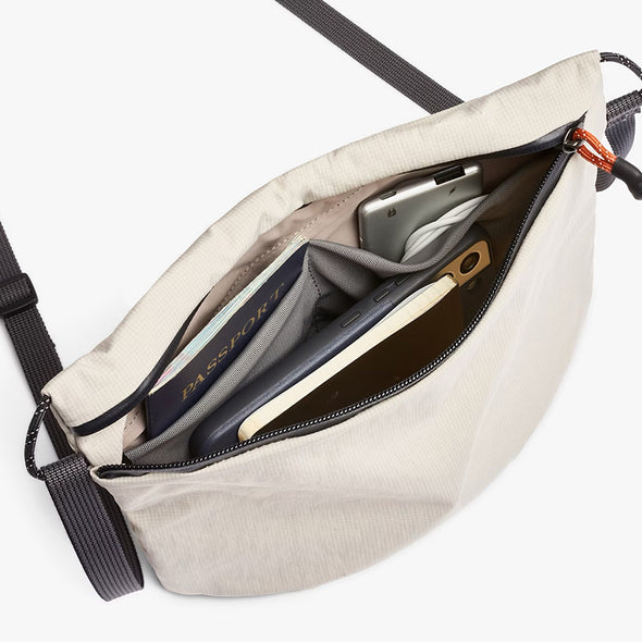 Beige crossbody bag with compartments containing a passport and phone on a white background