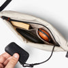 Beige crossbody bag with a hand holding a black phone case, on a light gray background
