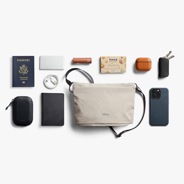 Collection of travel items including a beige bag, passport, phone, and other accessories on a white background.