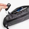 Gray crossbody bag with items inside, including a keychain and a pen, on a white background.