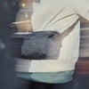 Person wearing a white jacket with a black mesh bag over their shoulder, blurred background