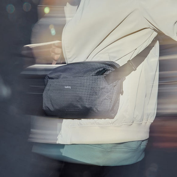 Person wearing a white jacket with a black mesh bag over their shoulder, blurred background
