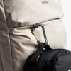 Close-up of a beige backpack with a black bag attached using a carabiner, featuring the brand 'bellroy'.