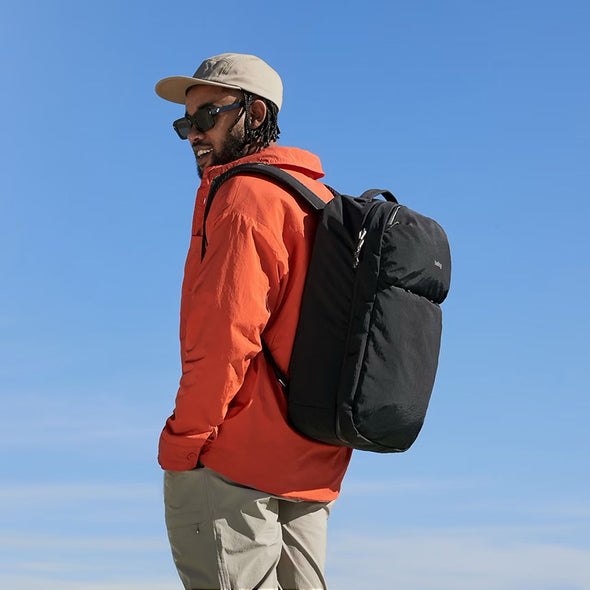 Man wearing an orange jacket and black backpack against a clear blue sky