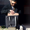 Man sitting on a bench with a black tote bag, holding a cardboard box.