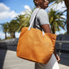 Person holding a copper tote bag with palm trees in the background