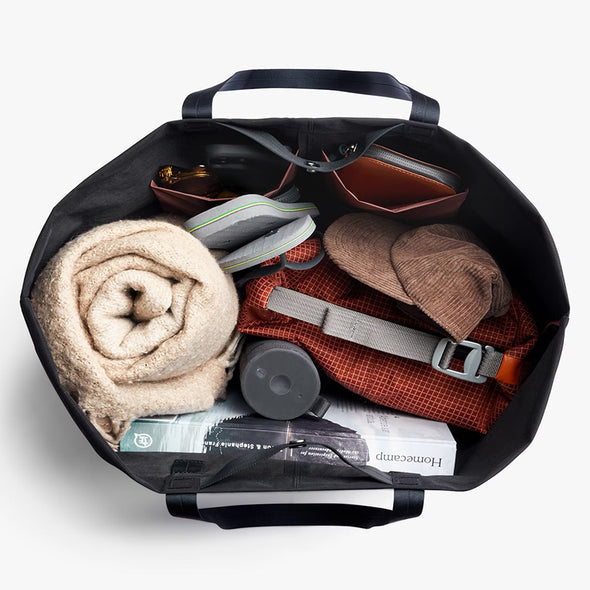 Black suitcase with travel items including a blanket, shoes, and a hat on a white background
