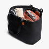 Black tote bag with various items including a backpack and clothes on a white background
