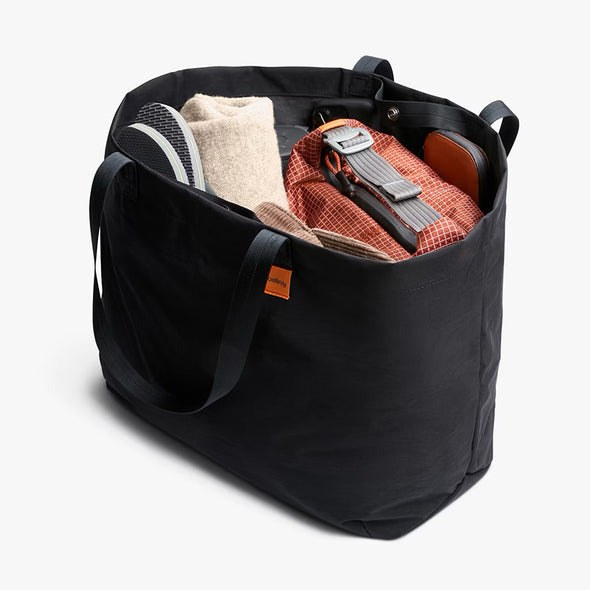 Black tote bag with various items including a backpack and clothes on a white background