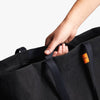 Person holding a black bag with an orange tag on a light gray background