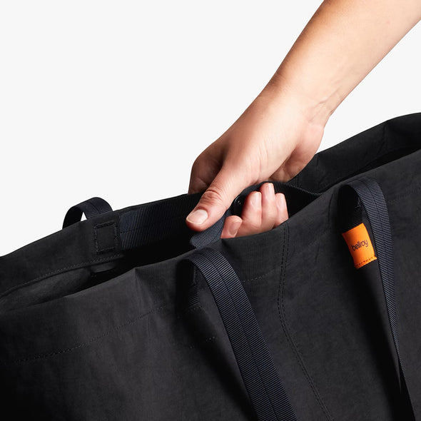 Person holding a black bag with an orange tag on a light gray background