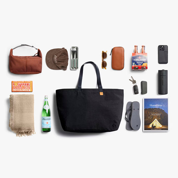 Black tote bag surrounded by various items on a white background