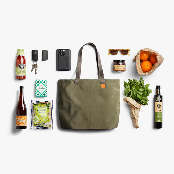 Green tote bag surrounded by various items on a white background