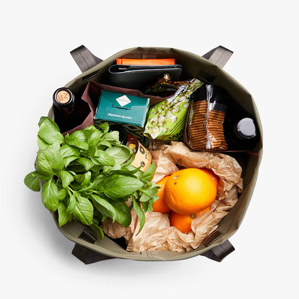 Open bag containing groceries including oranges, greens, and packaged items on a white background
