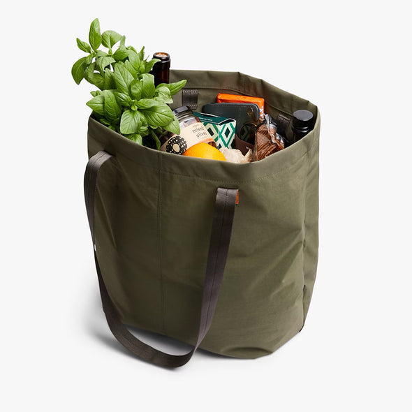 Green tote bag filled with groceries on a white background