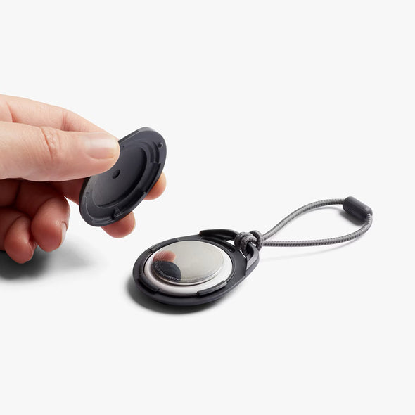 Hand holding a black and silver keychain device on a white background