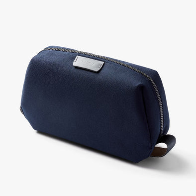 Navy blue toiletry bag with a brand logo on a light gray background
