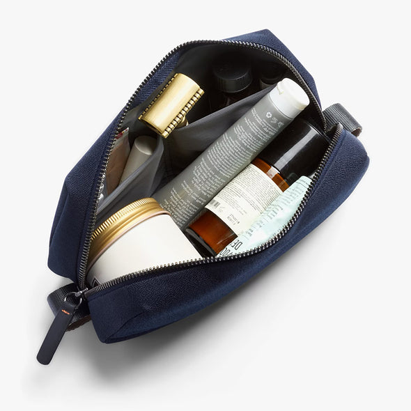 Open navy blue toiletry bag with various skincare products on a white background