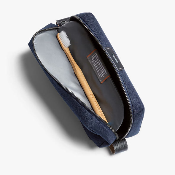 Navy toiletry bag with a toothbrush inside on a light gray background