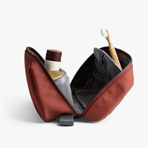 Open red toiletry bag with personal care items on a light gray background