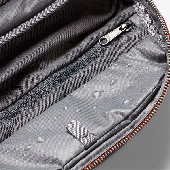 Gray bag with water droplets on the fabric, zipper, and brand logo.