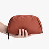 Brown toiletry bag held by a hand on a white background